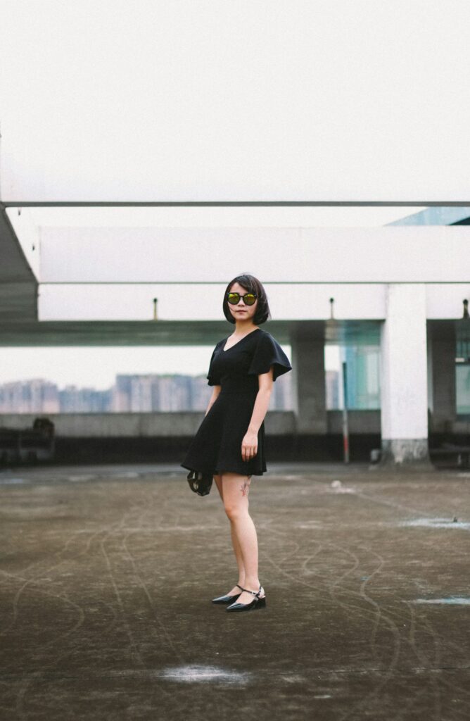 woman with glasses is posing at the camera wearing little black dress