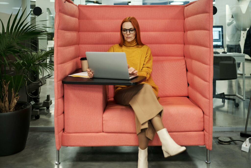  Businesswoman wearing ankle boots seated on a red couch, working on a laptop