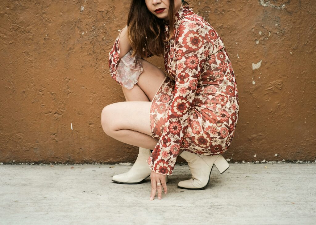 Crouched woman wearing red floral dress and white ankle boots