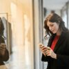 Woman wearing red top and black coat on her phone in front of store window