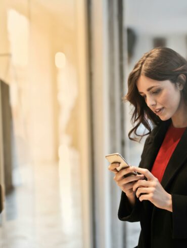 Woman wearing red top and black coat on her phone in front of store window