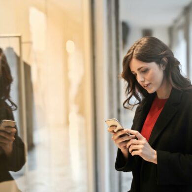 Woman wearing red top and black coat on her phone in front of store window