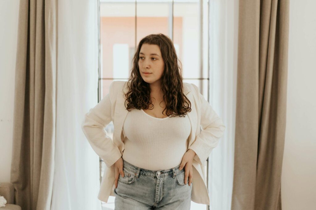 Woman wearing white bodysuit, cream blazer, and jeans